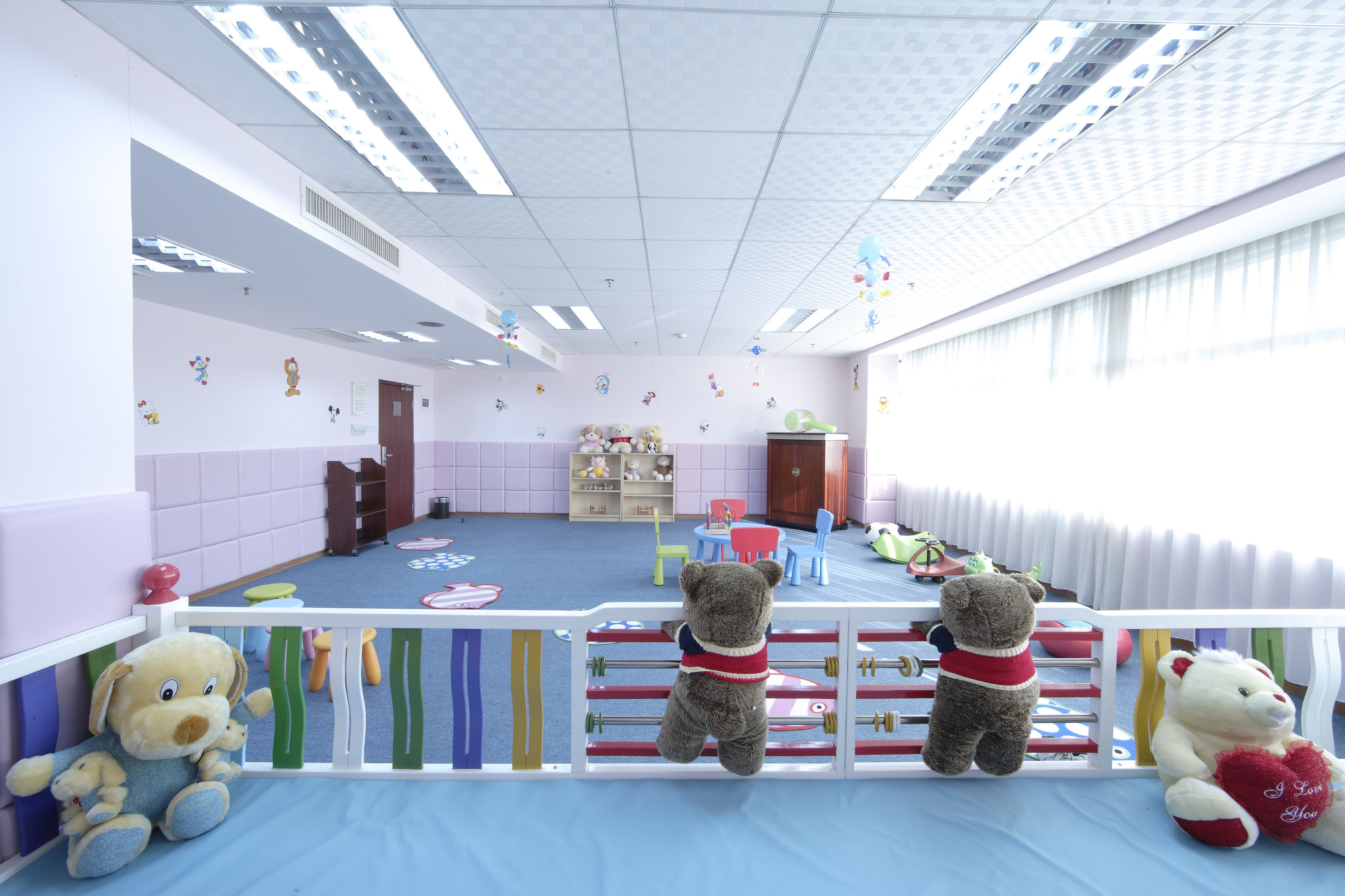 A children's playroom with a blue floor, white walls, and a white ceiling. There are toys and a teddy bear on the floor.