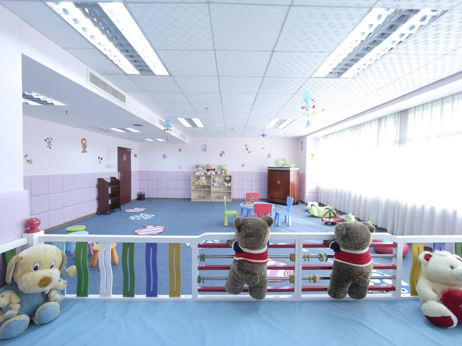 A children's playroom with a blue floor, white walls, and a white ceiling. There are toys and a teddy bear on the floor.