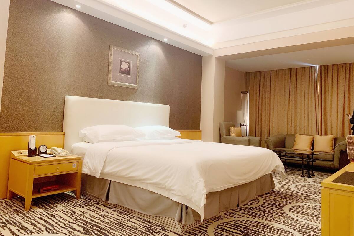 Une chambre d’hôtel avec un grand lit, une table de chevet avec un téléphone et une horloge, une chaise et un canapé.