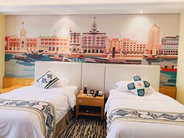 A hotel room with two beds, a mural of a cityscape on the wall, and a nightstand with a phone and a lamp.