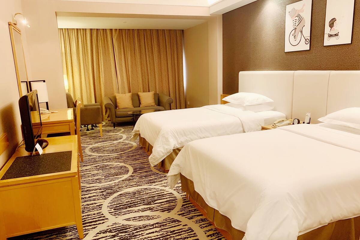 Une chambre d’hôtel avec deux lits, un bureau, une chaise, une télévision et une grande fenêtre avec des rideaux.
