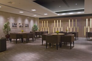 Un moderno vestíbulo de hotel con mesas y sillas redondas, plantas en macetas y cuadros en las paredes.