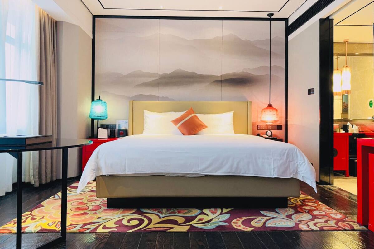 Une chambre d’hôtel avec un grand lit, une table de chevet, un bureau, une chaise et une salle de bain visible à travers une porte ouverte.