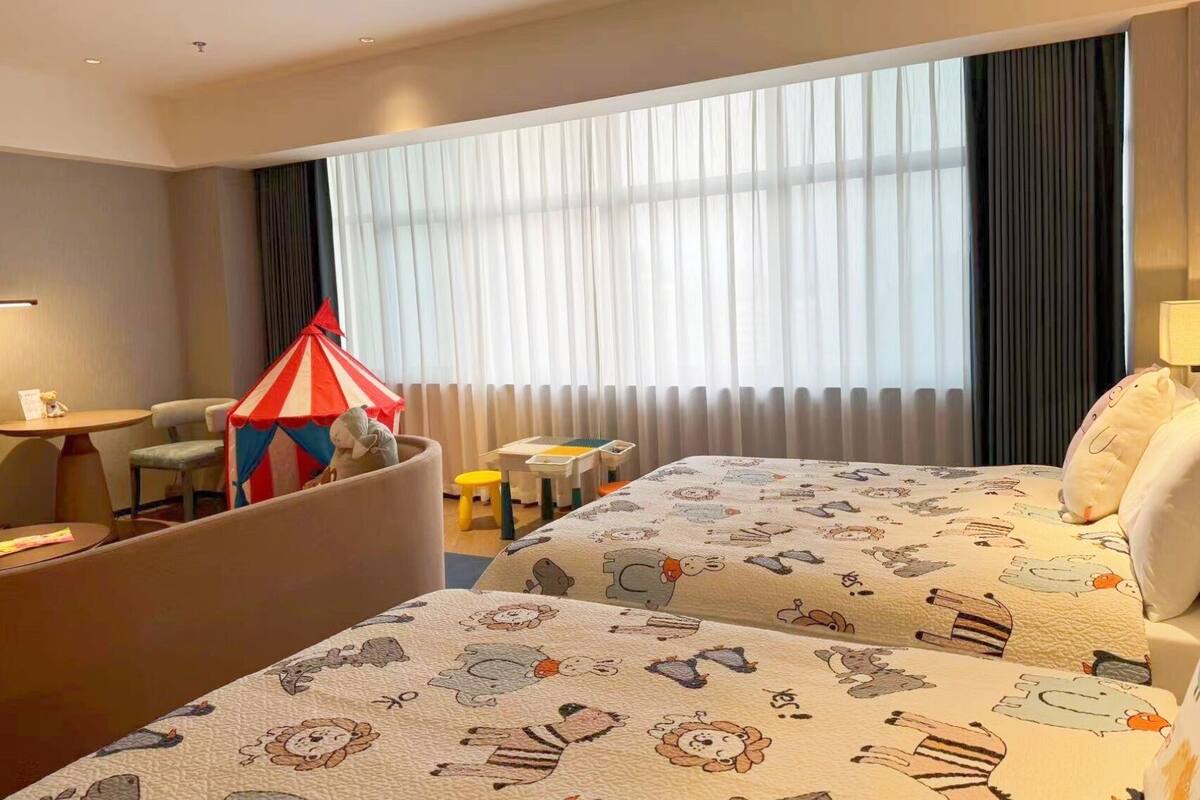 Une chambre d’hôtel avec deux lits, une petite table, une chaise, une tente et une fenêtre avec des rideaux.