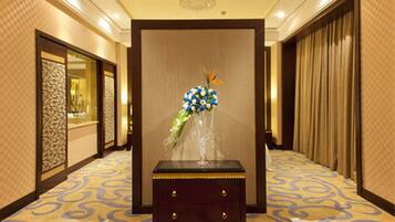 A hotel lobby with a decorative vase of flowers on a wooden table, patterned carpet, and a chandelier.