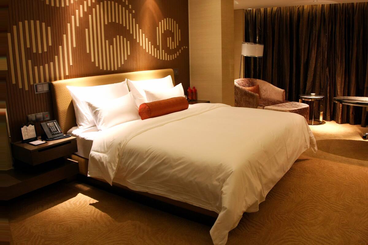 Une chambre d’hôtel avec un grand lit, une table de chevet avec un téléphone et un bloc-notes, une chaise, une petite table et une lampe.