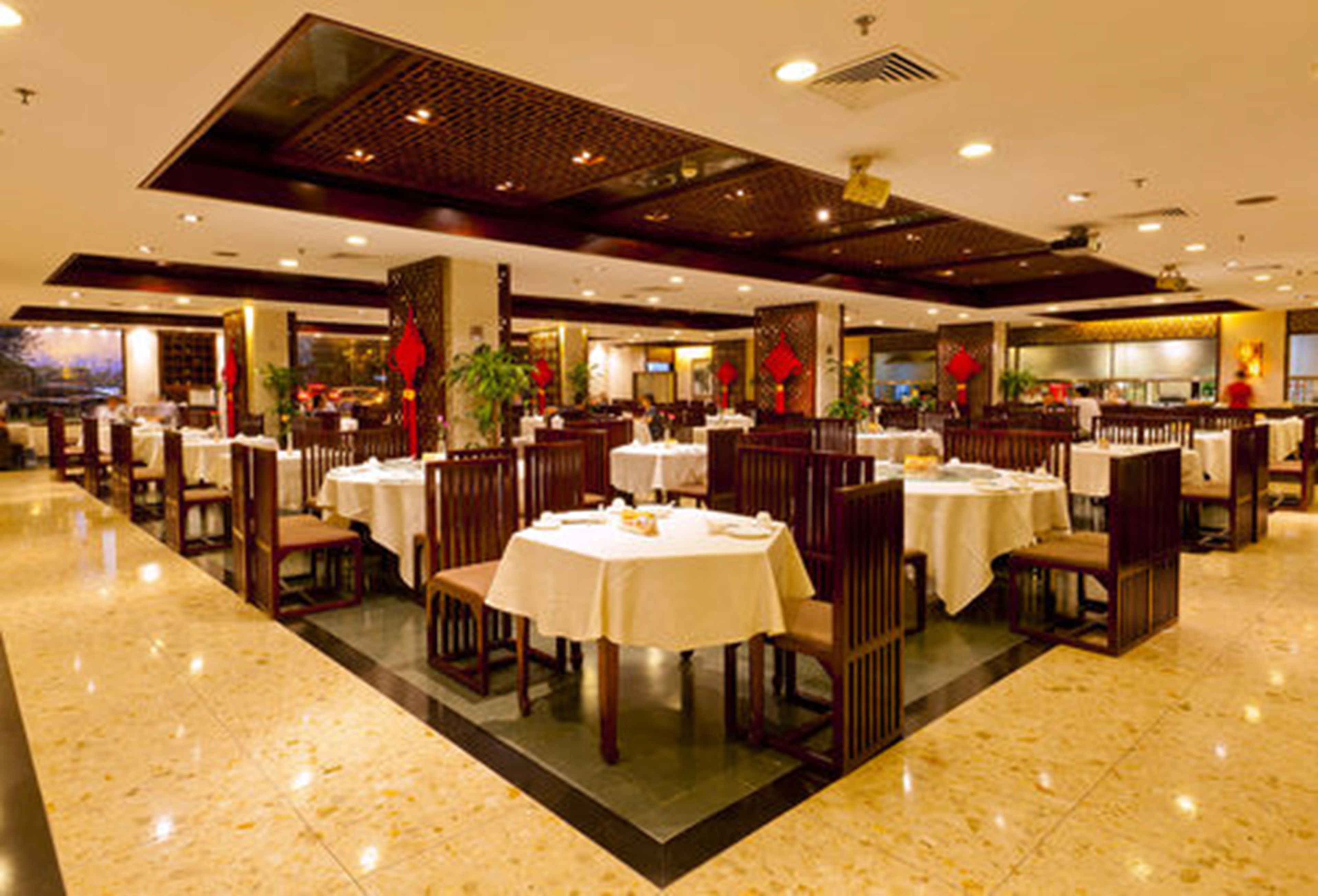 Un restaurante espacioso con varias mesas y sillas, piso pulido y un diseño de techo moderno.
