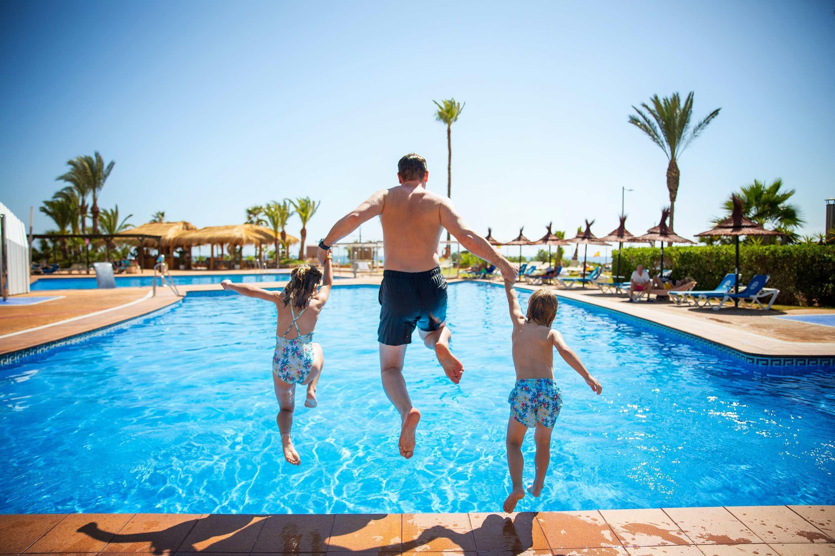 Een zwembad waar een man en twee kinderen in het water springen.