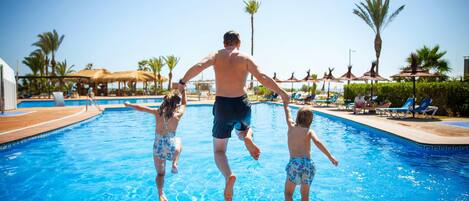 Une piscine dans laquelle un homme et deux enfants sautent à l’eau.
