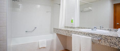 A bathroom with a white bathtub, a sink with a granite countertop, and a mirror above the sink.