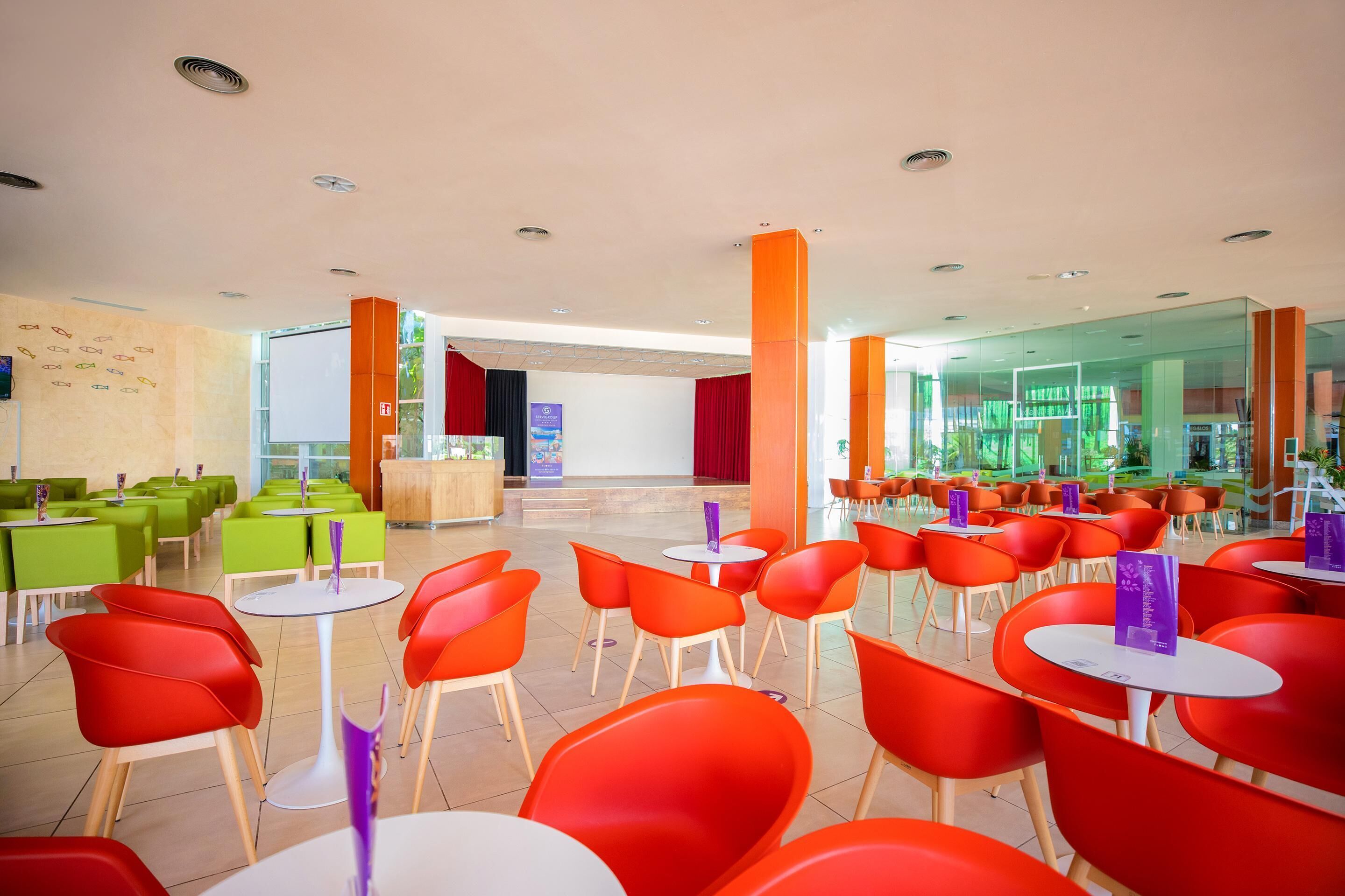 A spacious indoor area with multiple seating arrangements, including tables and chairs, and a reception area in the background.
