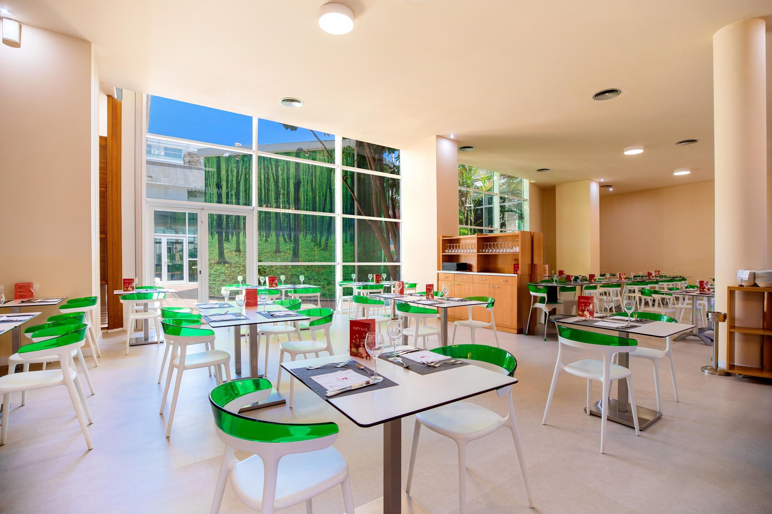 Un comedor amplio con mesas y sillas, ventanas grandes y vistas a zonas verdes.