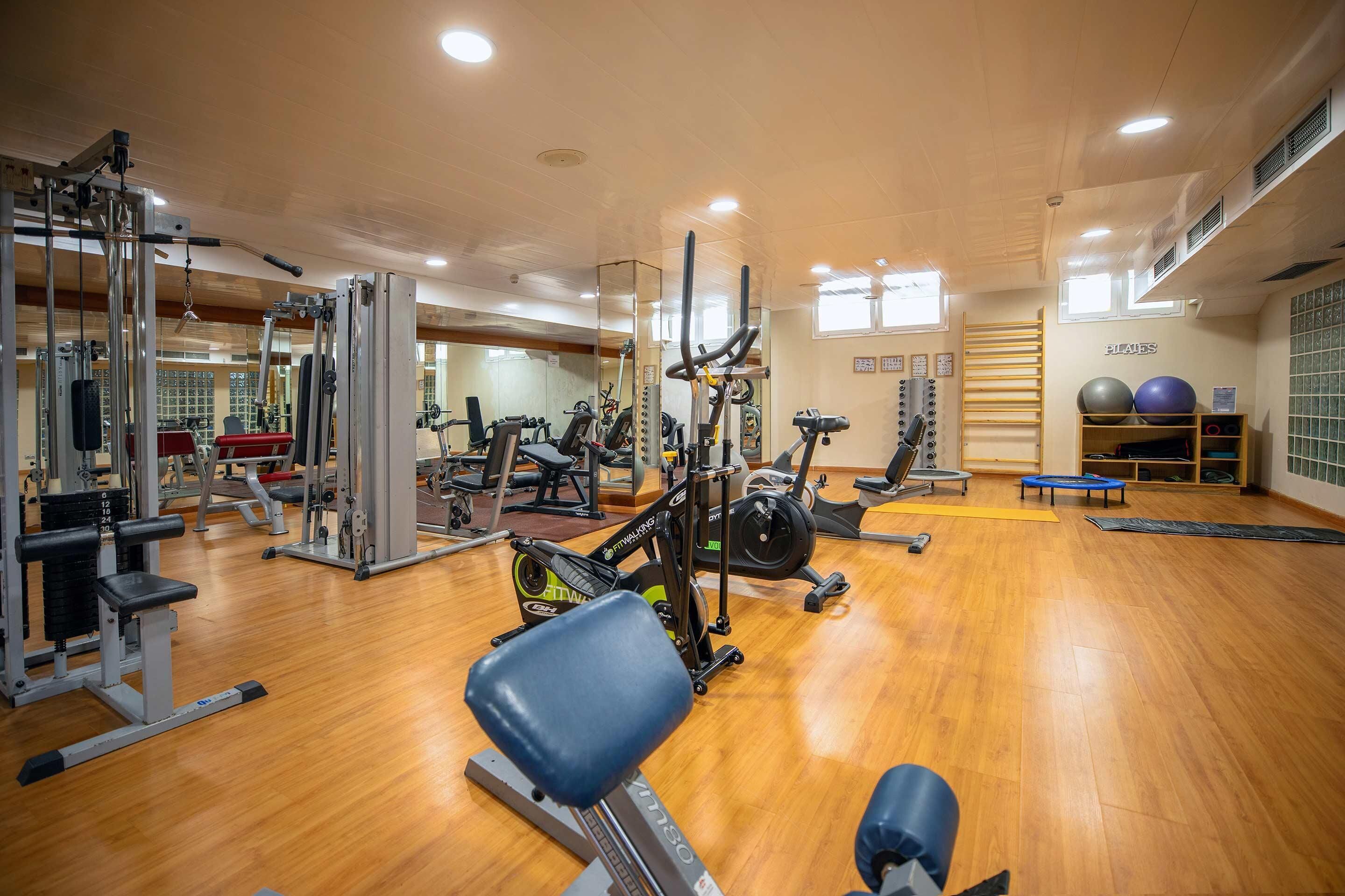 Un gimnasio con diferentes equipos de ejercicio, un espejo grande y piso de madera.