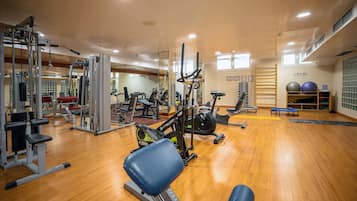 Un gimnasio con diferentes equipos de ejercicio, un espejo grande y piso de madera.