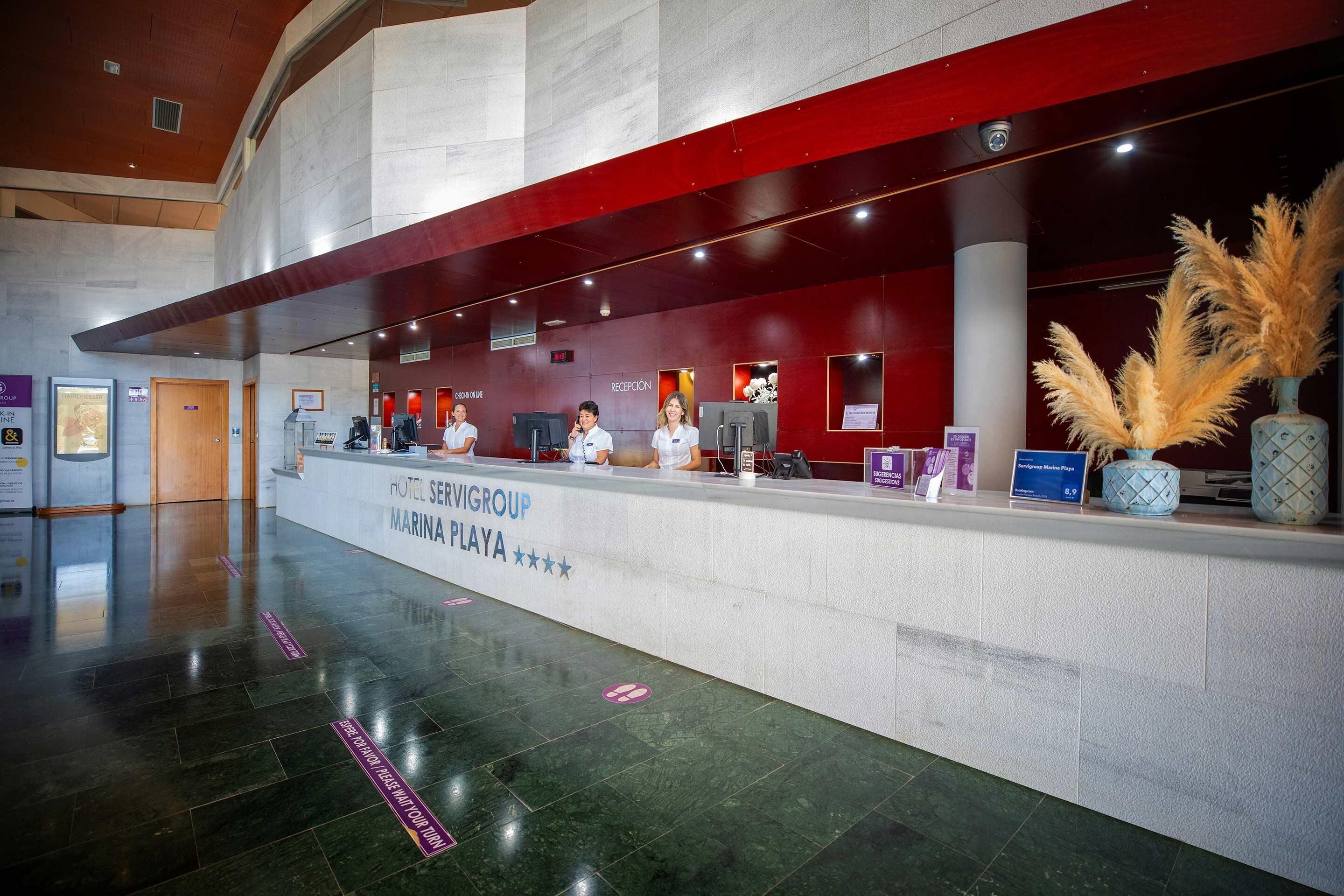 A hotel reception area with a modern design, featuring a reception desk, staff, and a decorative plant.