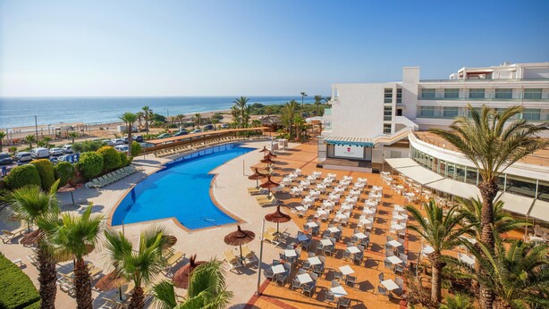 Un resort con una gran piscina, zona de playa y un edificio de varios pisos.