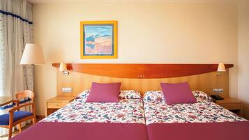 Een tweepersoonsbed met bloemenbeddengoed, een houten hoofdbord, twee nachtkastjes, een stoel en een nachtkastje met een lamp.