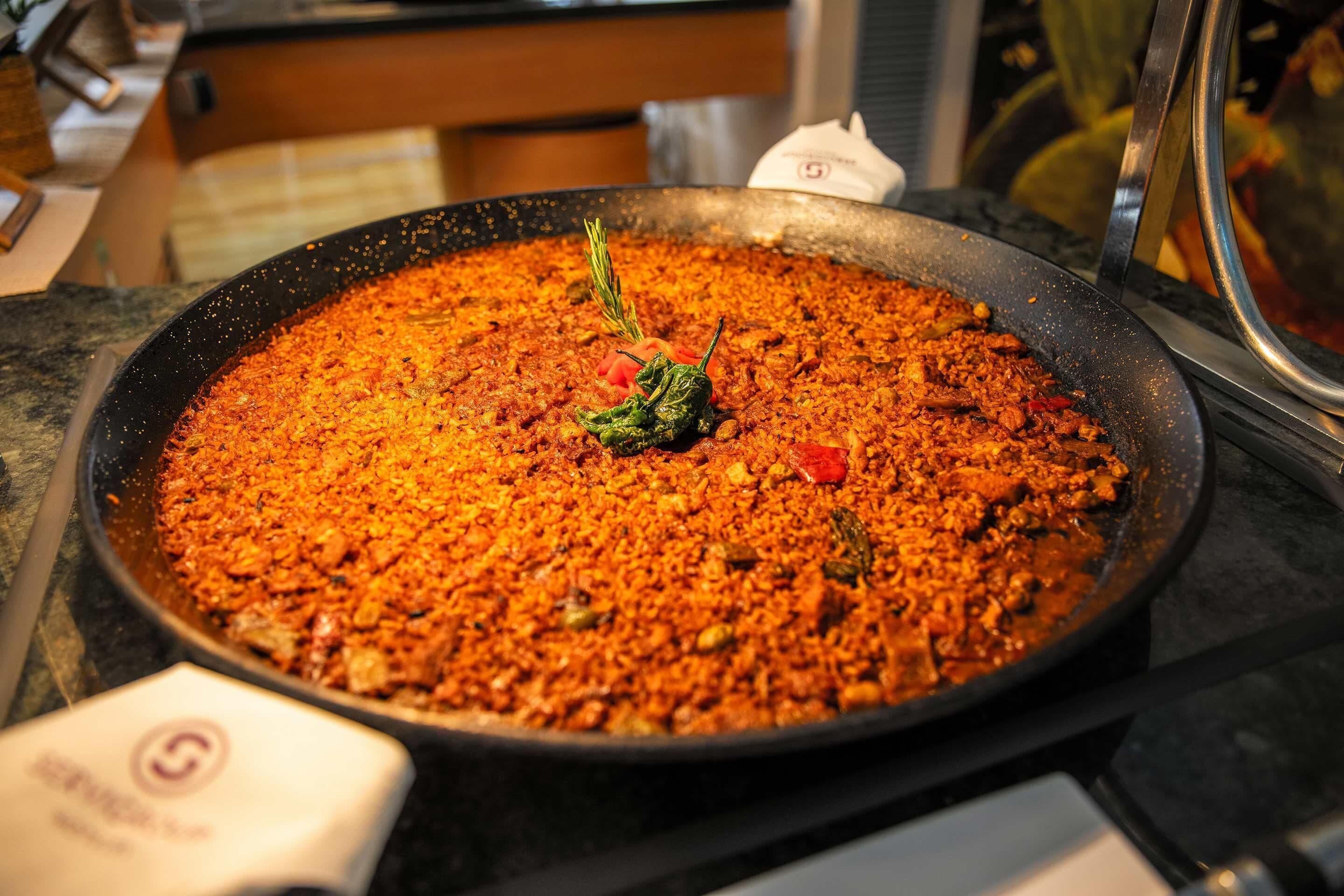Una sartén grande llena de un plato, posiblemente una paella, sobre una hornilla.