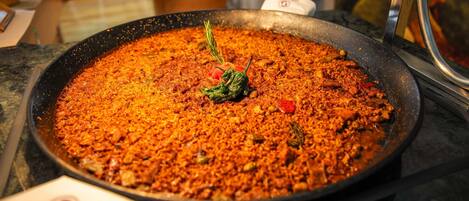 Una sartén grande llena de un plato, posiblemente una paella, sobre una hornilla.