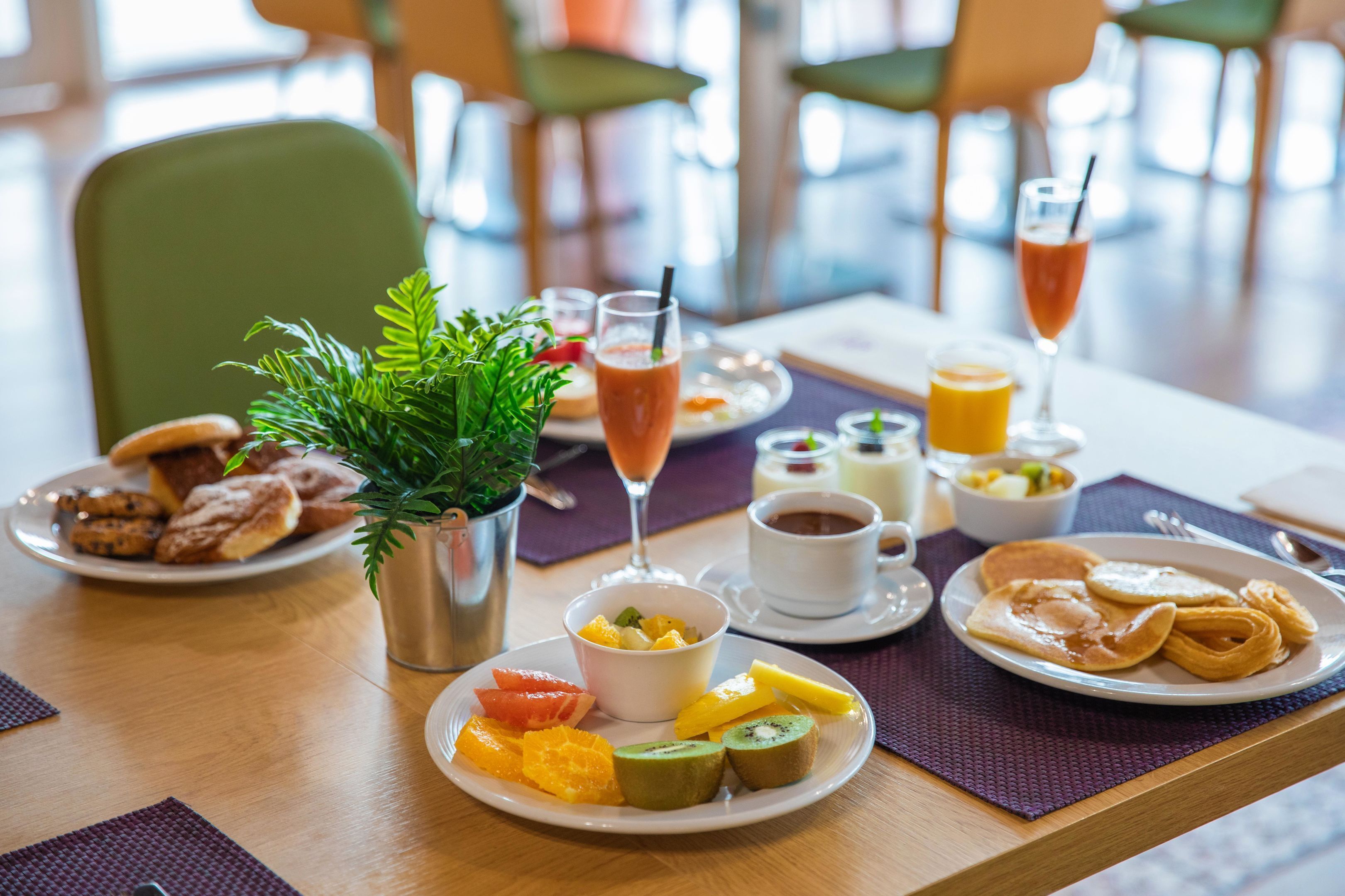 A breakfast setting with a variety of foods, including fruits, pastries, and beverages on a wooden table.
