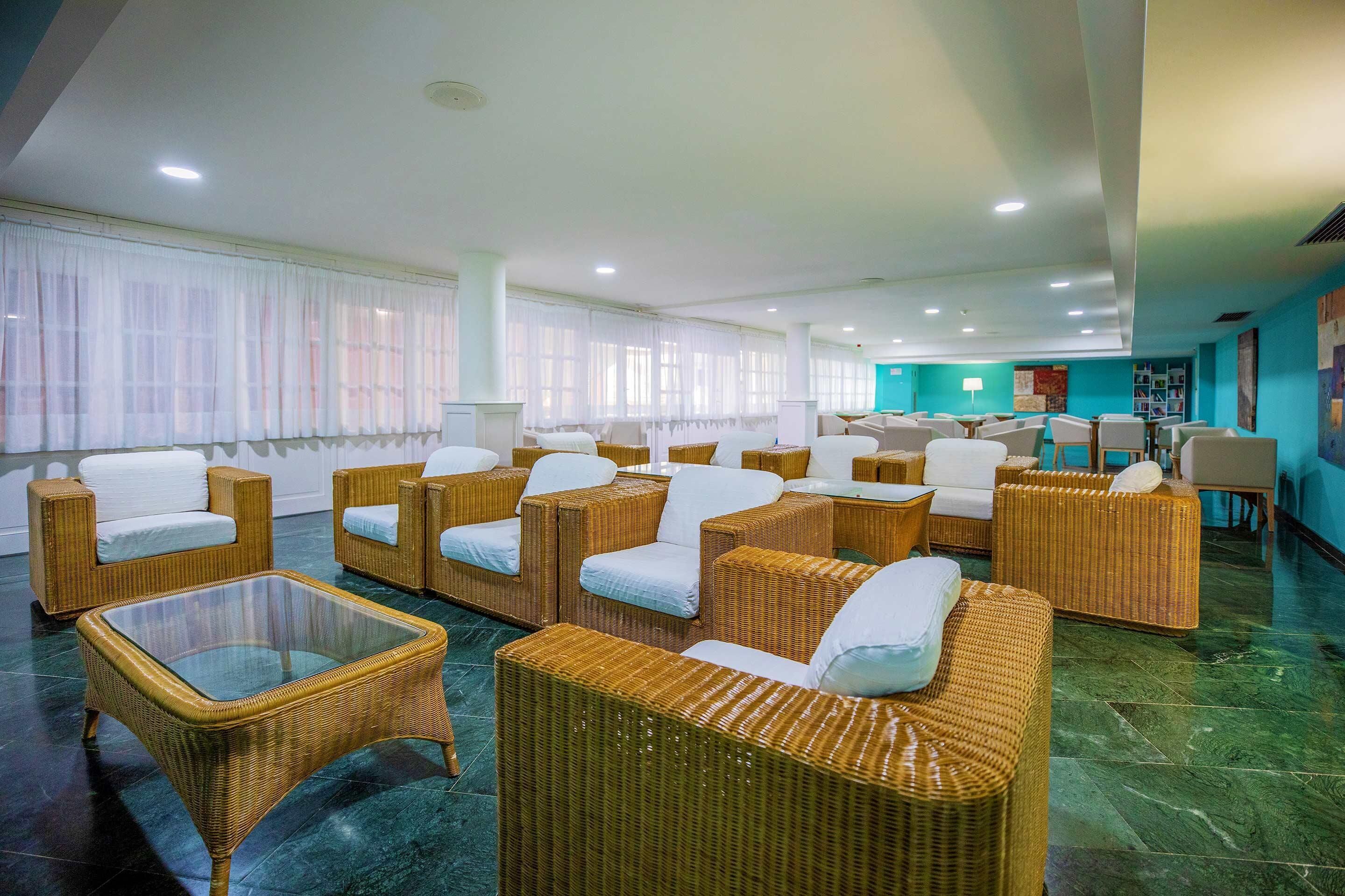 Vestíbulo de hotel con muebles de mimbre, una mesa de centro de vidrio y una pared de acento color verde azulado.