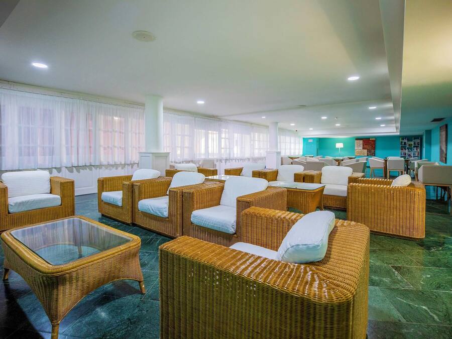 Vestíbulo de hotel con muebles de mimbre, una mesa de centro de vidrio y una pared de acento color verde azulado.