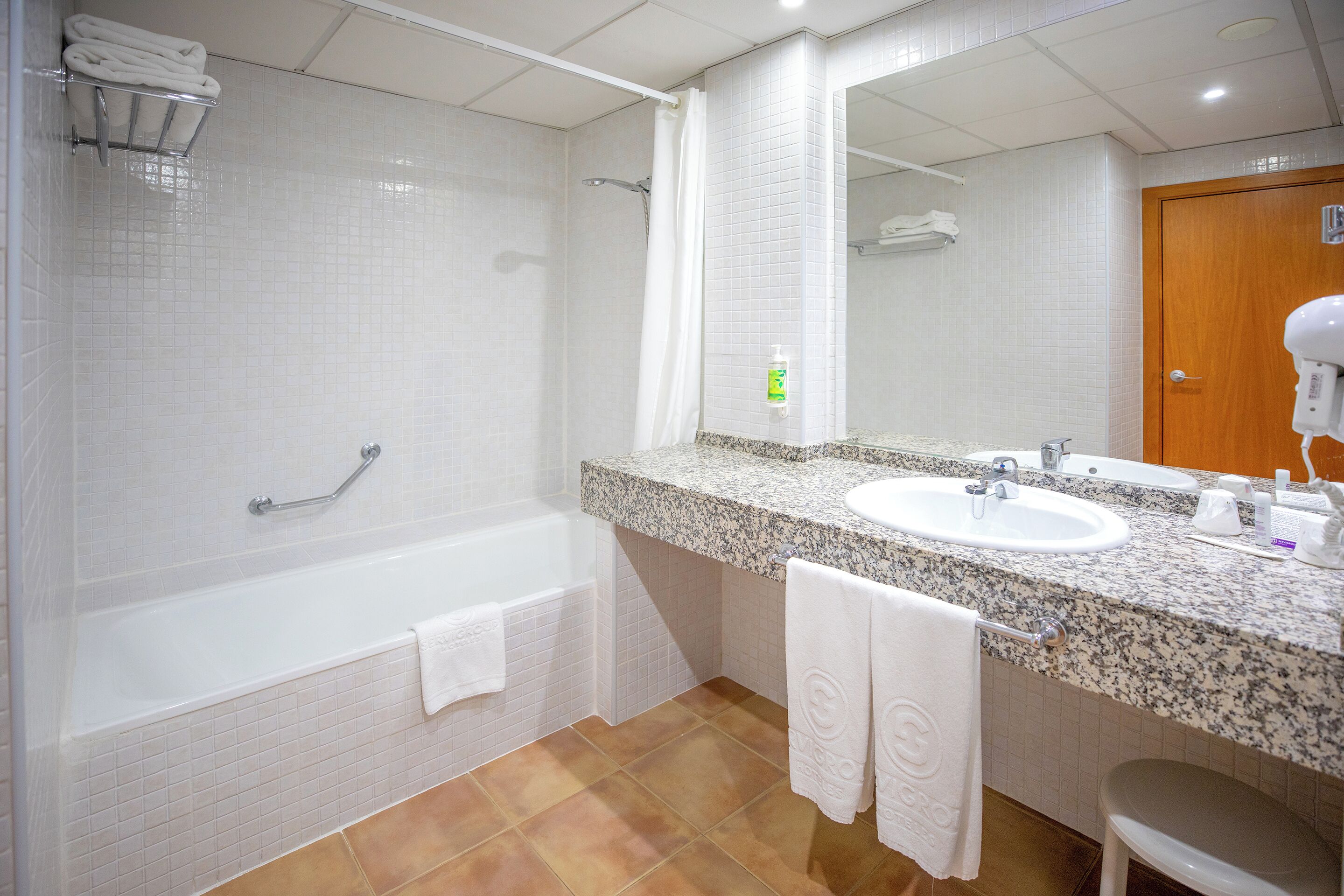 Un baño con una bañera blanca, un lavabo y un espejo grande. Hay toallas colgadas en la pared y una cortina de ducha.