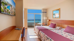 Habitación de hotel con cama, escritorio, silla, mesa y vista al océano.