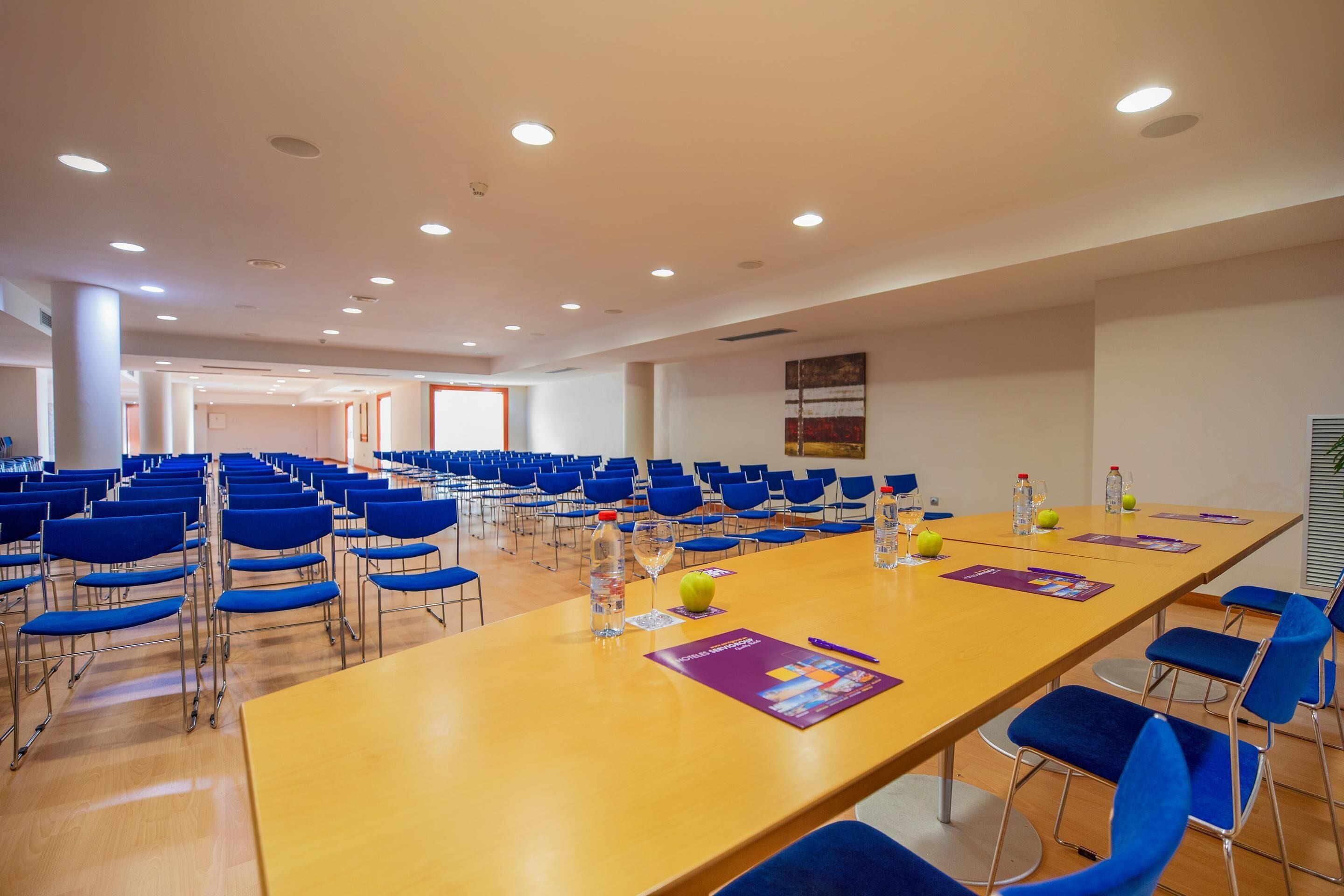 Un salón de conferencias con una larga mesa, sillas azules y suelo de madera.