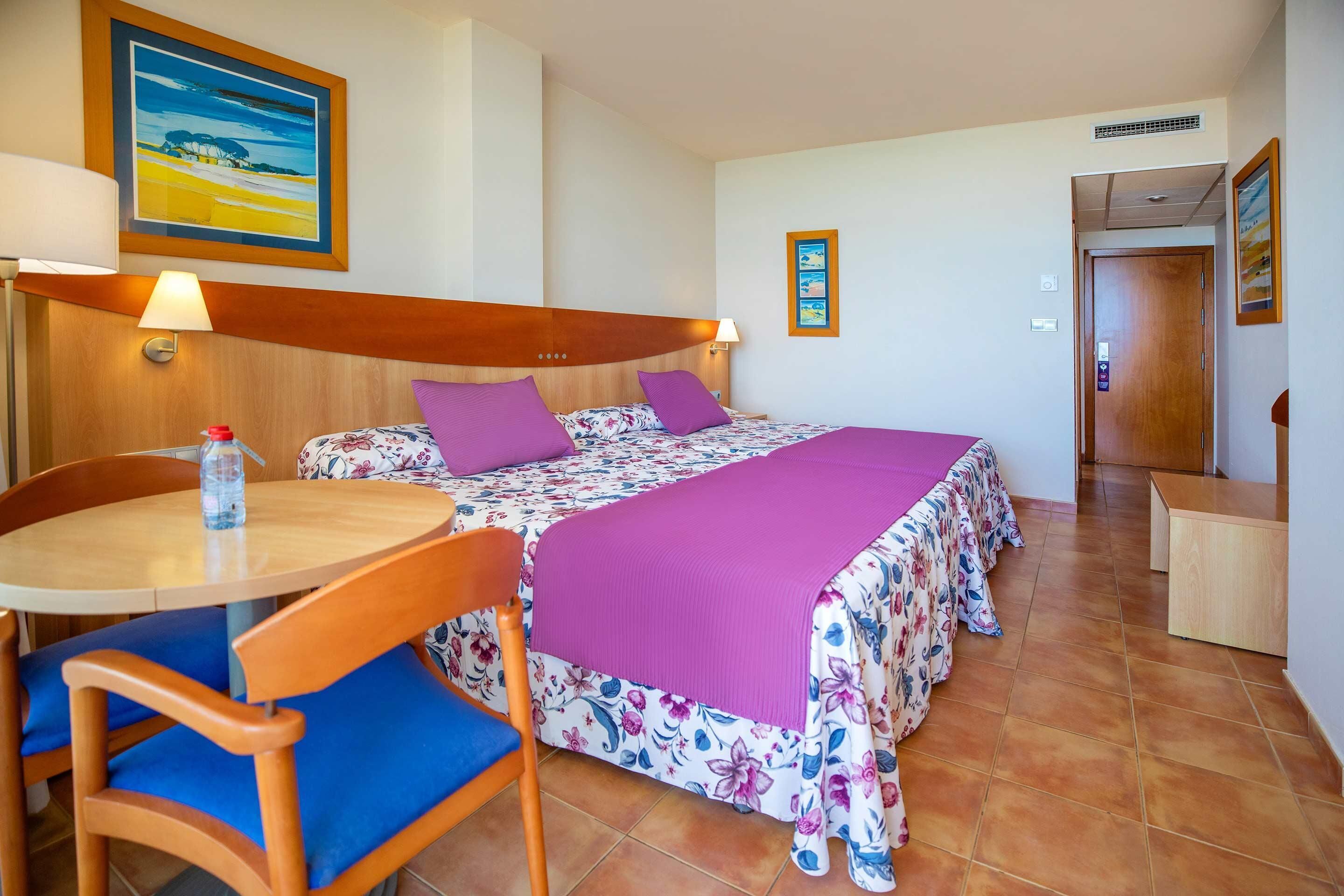 A hotel room with a bed, a table, chairs, and a small desk.