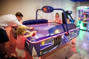 Ein Pooltisch-Spielbereich mit Neonreklame, einer Krabschere-Greifmaschine und einer Person beim Spielen.