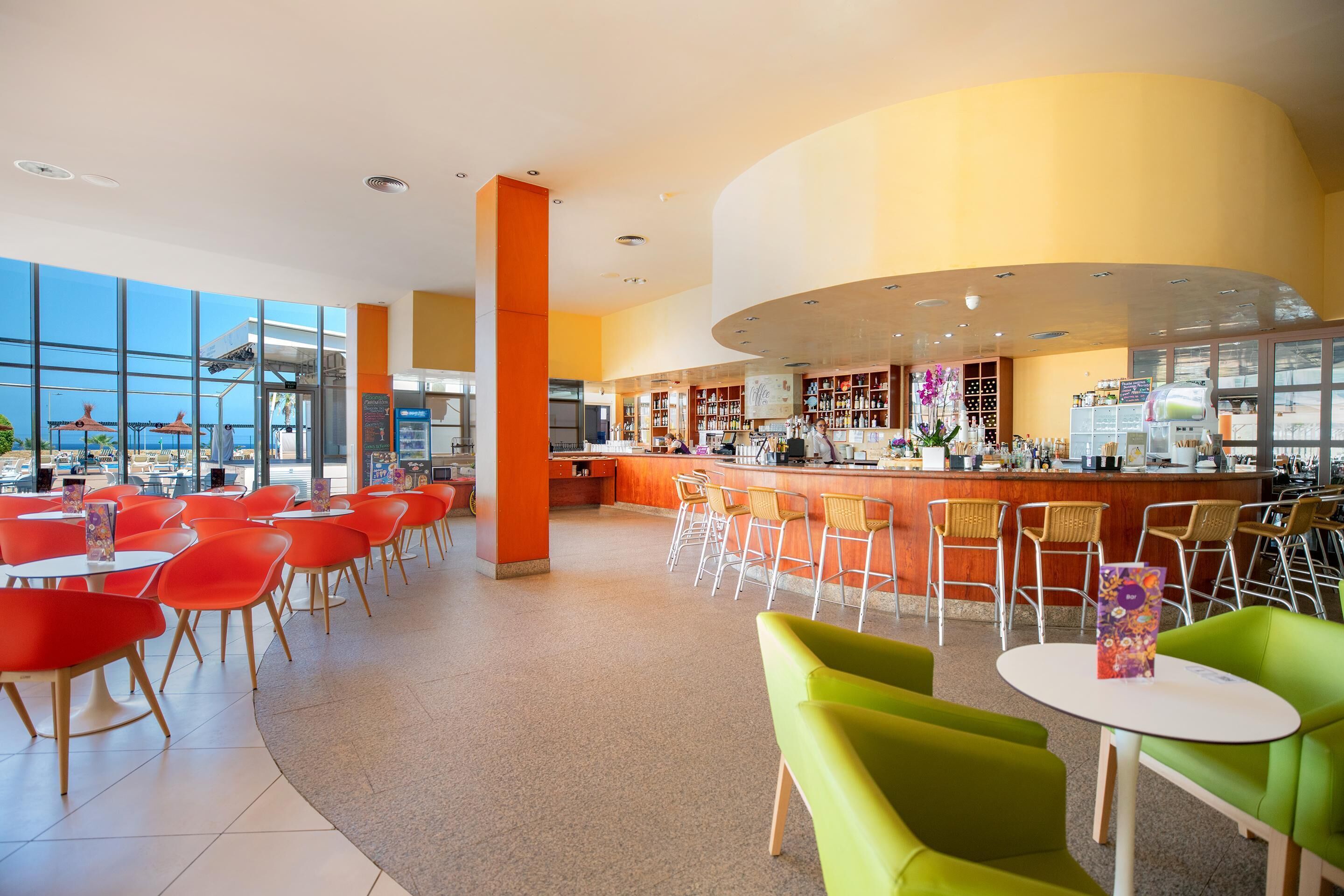 A modern restaurant with a bar area, high ceilings, and large windows offering a view.