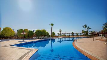 A swimming pool with a tiled deck, palm trees, and a clear blue sky.