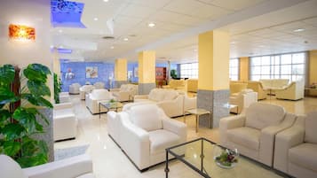 A spacious lobby with multiple seating areas, a reception desk, and a large window providing natural light.