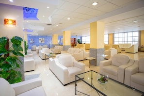 A spacious lobby with multiple seating areas, a reception desk, and a large window providing natural light. - Hotel Servigroup Nereo (Benidorm)