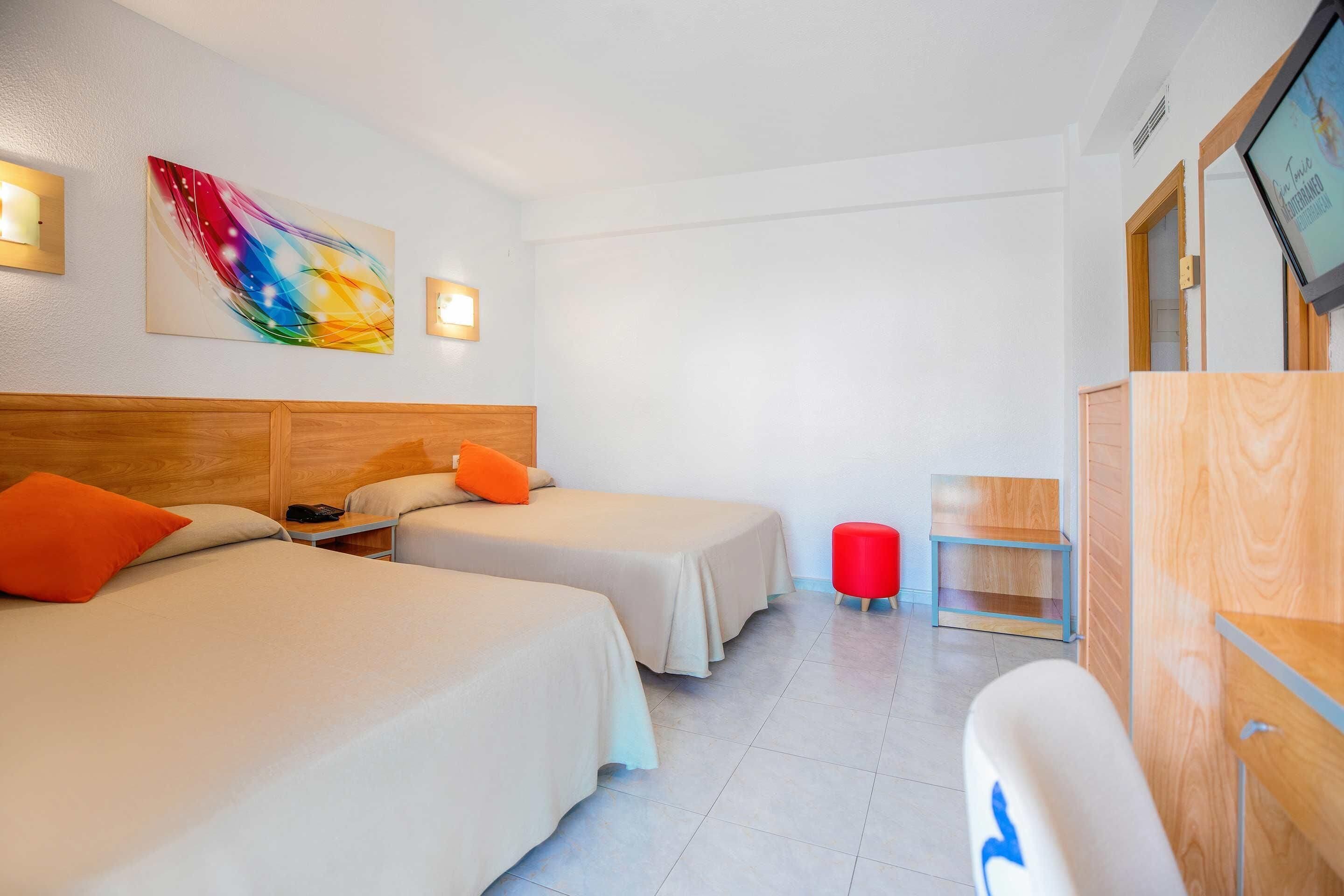 A hotel room with two beds, a TV, a wooden headboard, a colorful abstract painting, and a red stool.