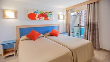 Ein Hotelzimmer mit zwei Betten, einem Nachttisch, einem Sessel und einem Balkon mit Vorhängen, sowie einem Gemälde an der Wand.