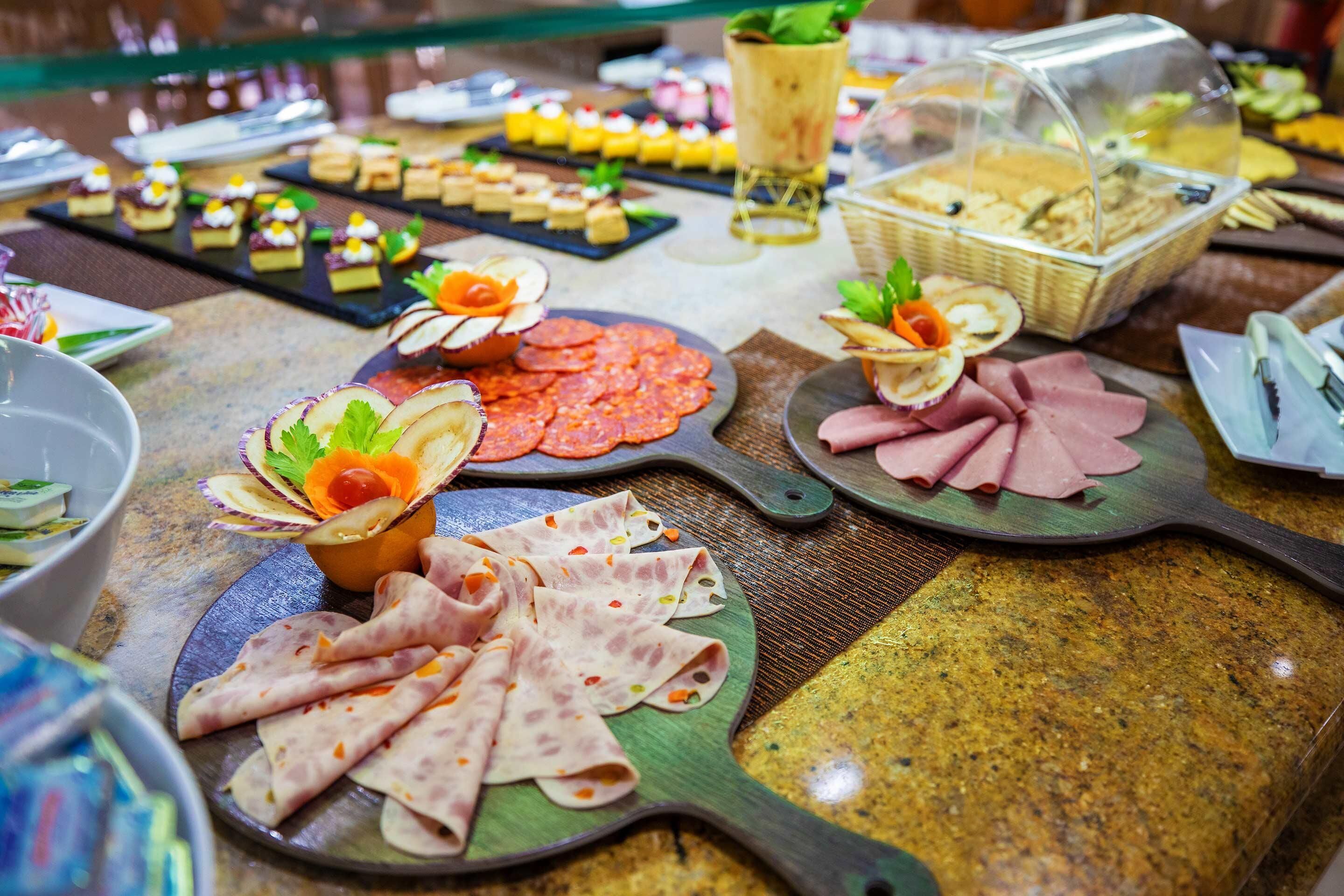 A buffet with various food items including sliced meats, cheeses, and pastries.