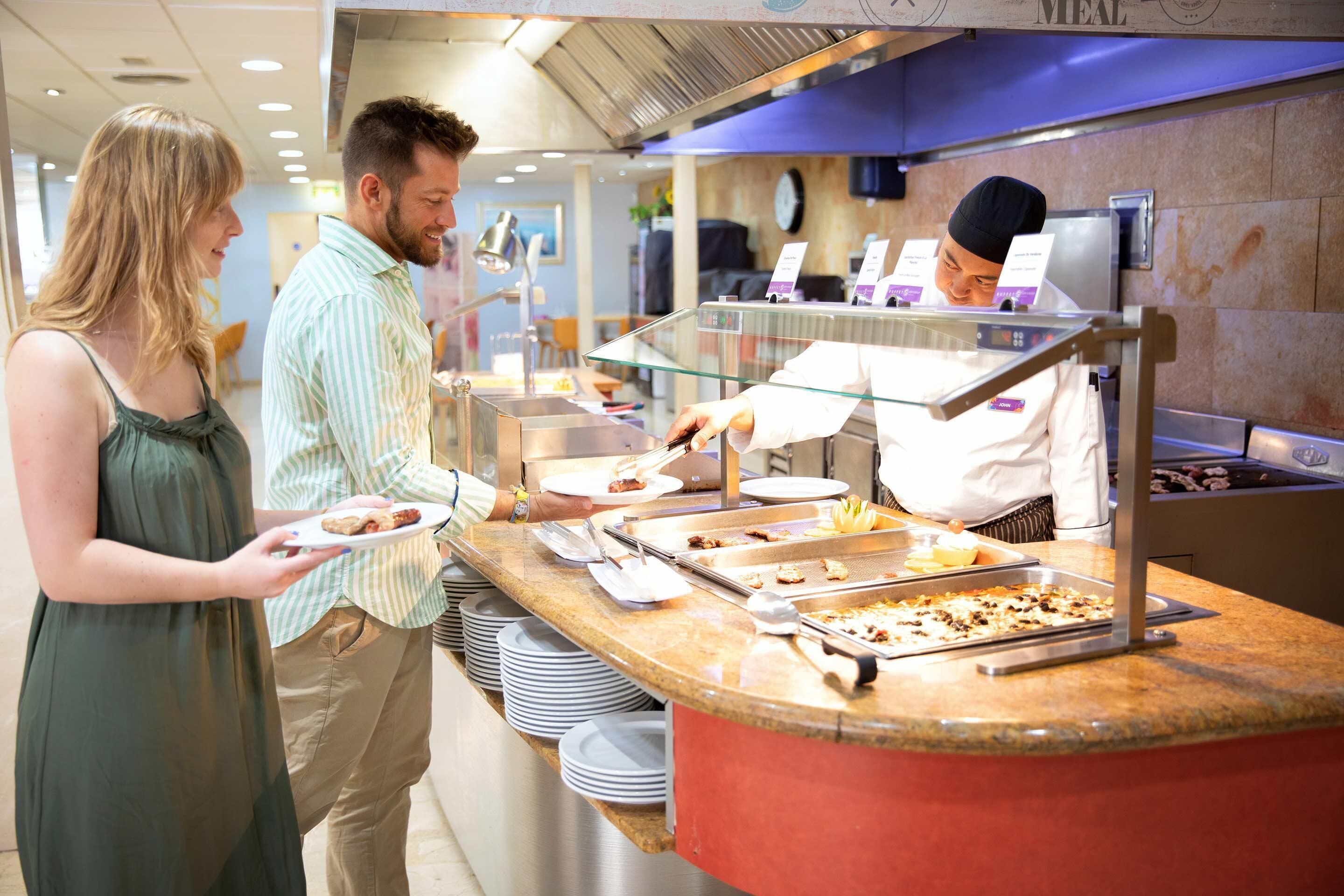A buffet counter with various food items and a staff member serving food.