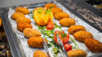 Bandeja con crujientes croquetas de color dorado, dispuestas sobre un papel de periódico, adornadas con tomates cherry, perejil y una rodaja de pimiento.