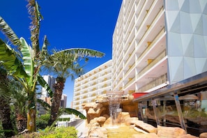 A hotel with a waterfall feature, palm trees, and a modern building facade.