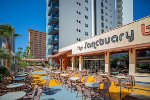 An outdoor seating area with wicker chairs and tables, a building with balconies, and a sign that reads "The Sanctuary". - Hotel Servigroup Orange (Benidorm)