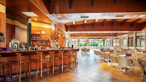 A spacious bar area with a high ceiling and wooden beams, featuring a bar counter with stools and a variety of bottles. - Hotel Servigroup Orange (Benidorm)