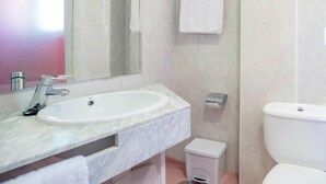 A bathroom with a sink, mirror, towel rack, toilet, and trash bin. - Hotel Servigroup Orange (Benidorm)