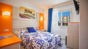 A hotel room with a bed, a desk, and a window with a view of buildings. - Hotel Servigroup Orange (Benidorm)