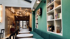 Ein modernes Interieur mit runden Tischen und Stühlen, einer grünen Akzentwand und einem Bücherregal voller Bücher.