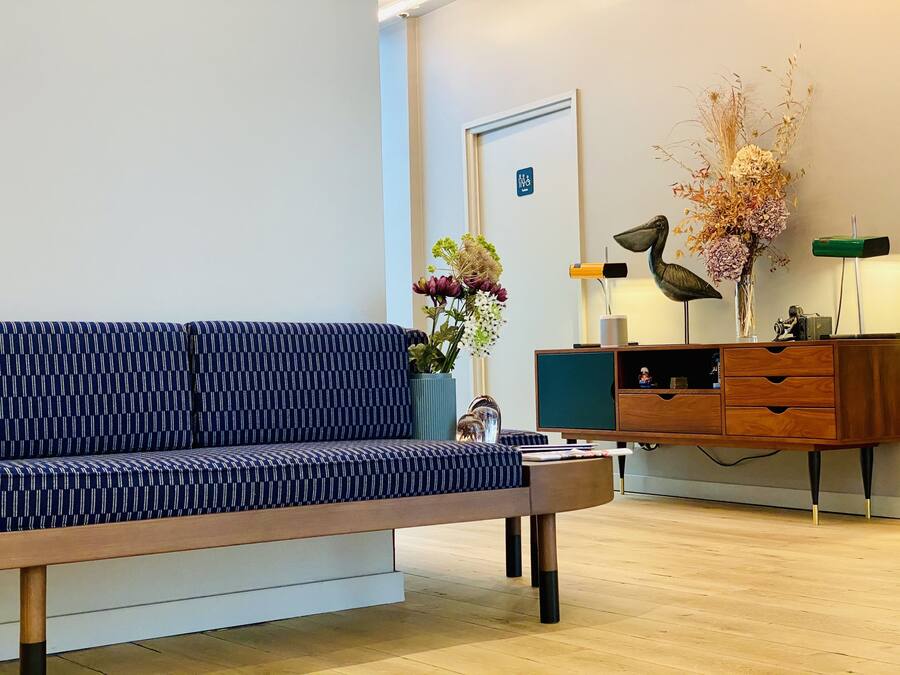 A modern living room with a patterned sofa, a wooden coffee table, a sideboard with drawers, and a vase with flowers.