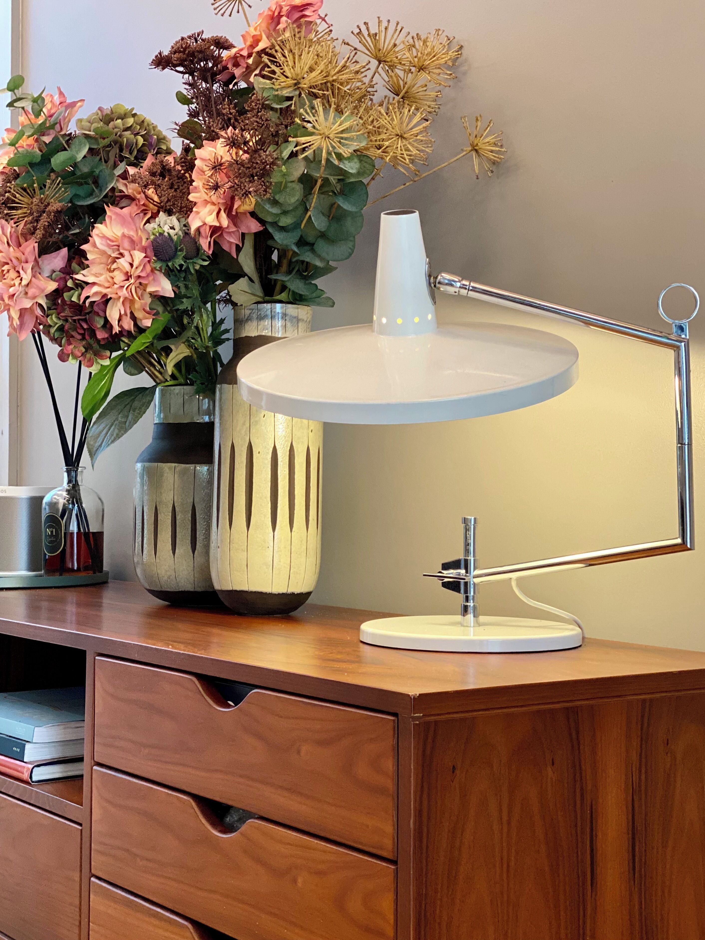 Een bureau met een witte bureaulamp, een vaas met bloemen en een fles.