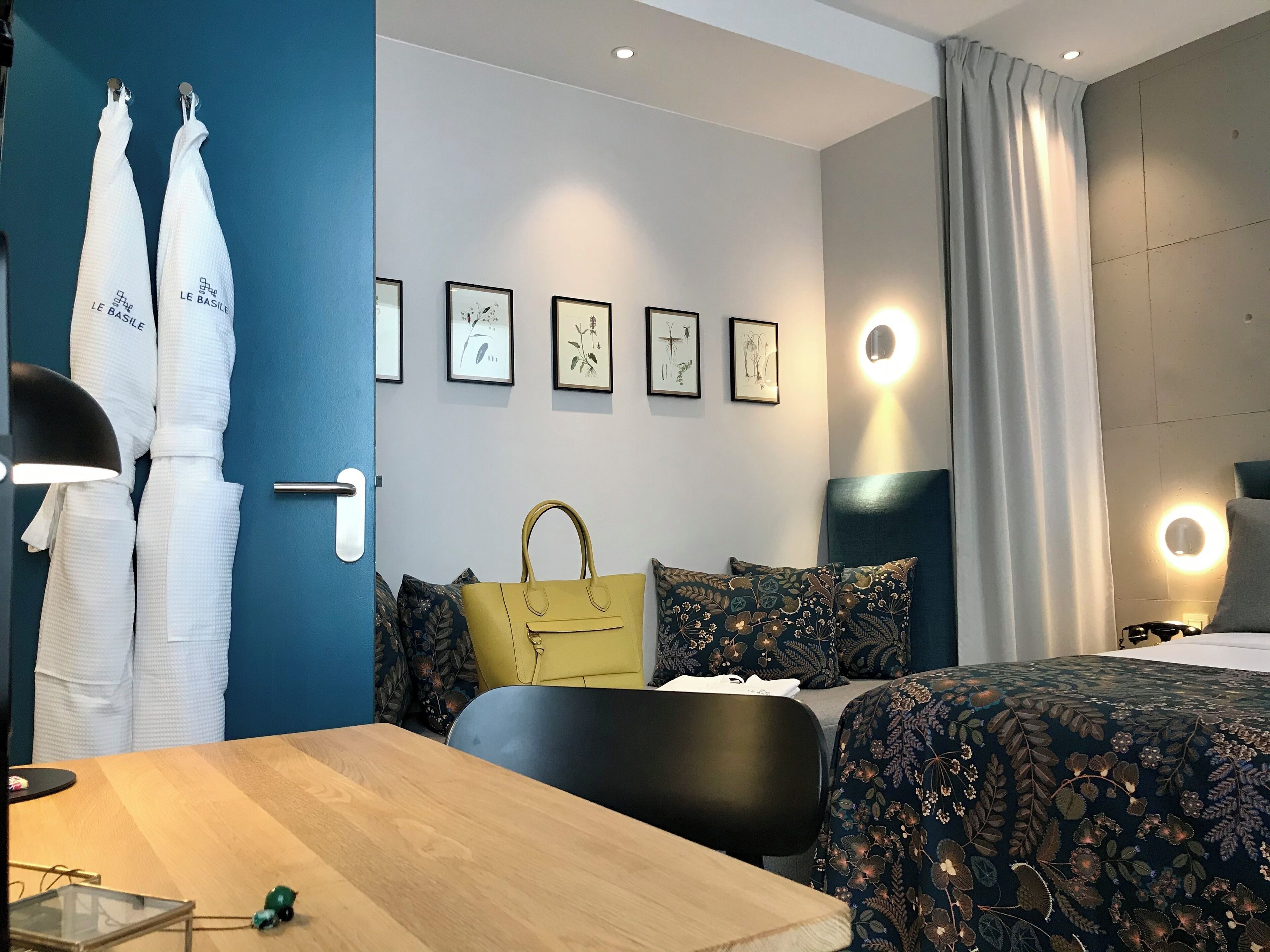 A hotel room with a bed, a desk, a chair, a table, a lamp, a handbag, and a wardrobe with towels.