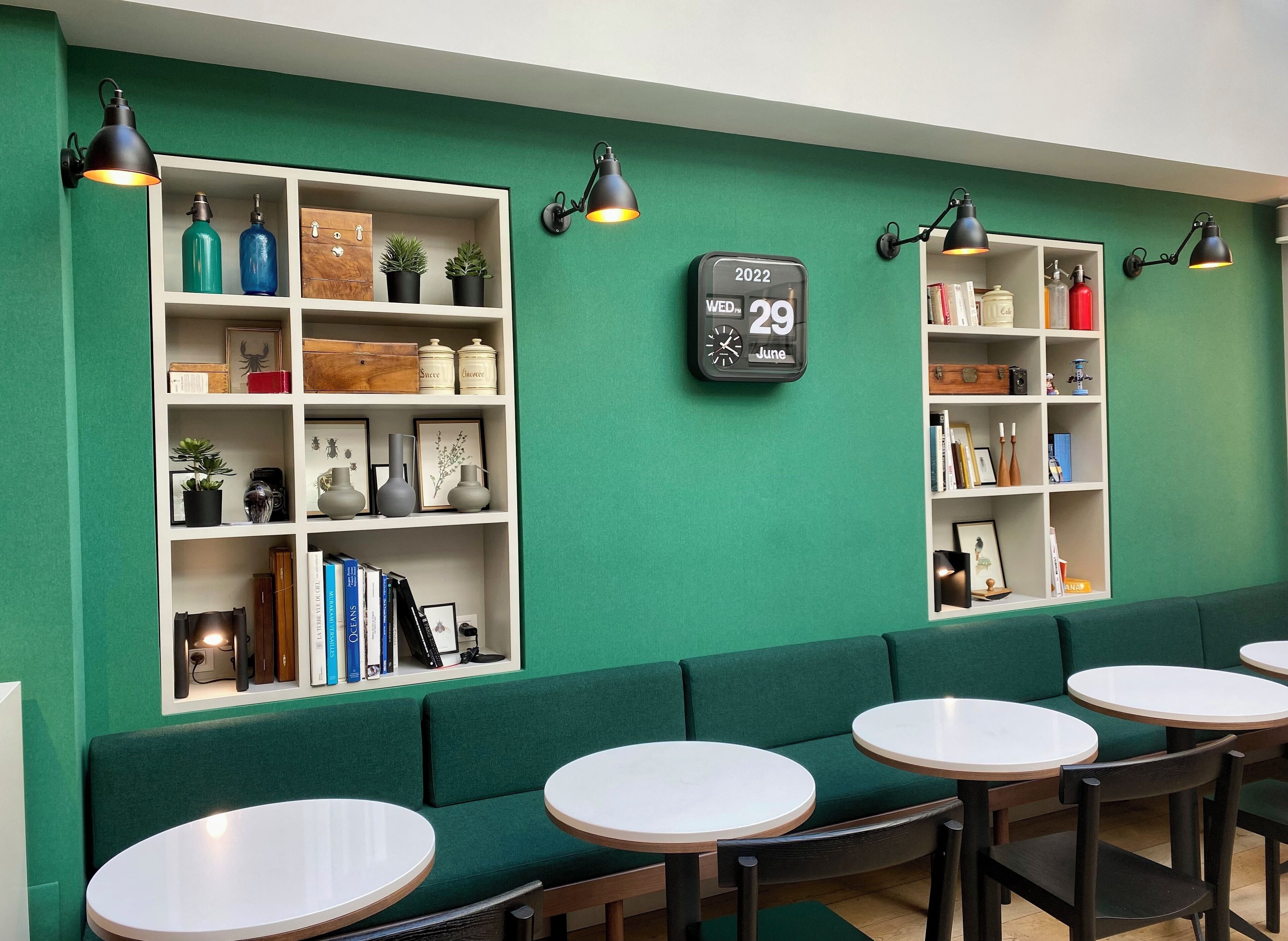A green-themed cafe with white shelves, books, and a clock displaying the date.